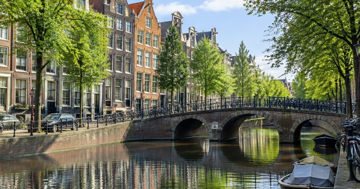 Tree-lined canal, arched bridge and narrow gabled houses reflected in water