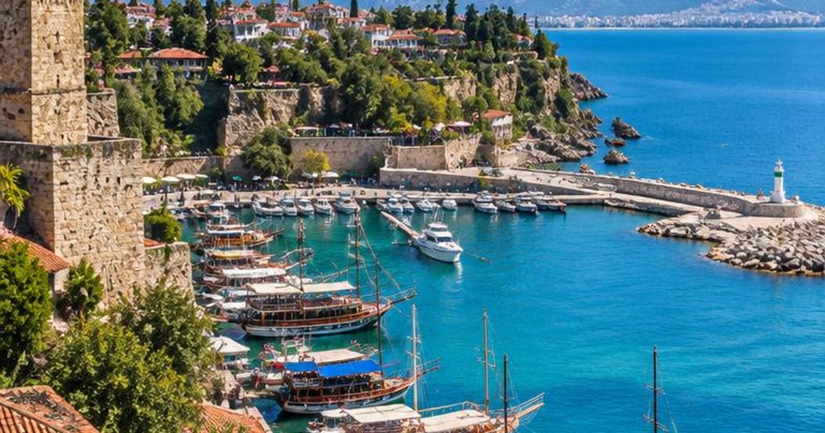 A compact harbour beneath old stone buildings, backed by mountains and blue sea