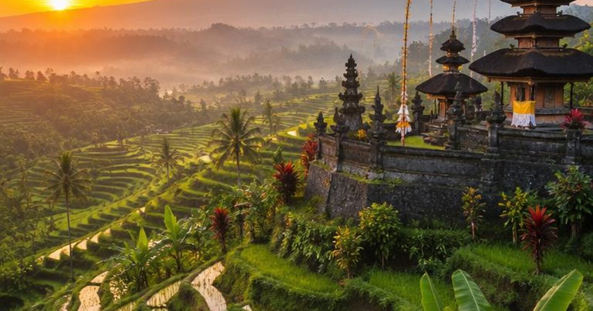 Terraced green fields, a tiered temple-like structure and a distant volcanic cone at sunrise