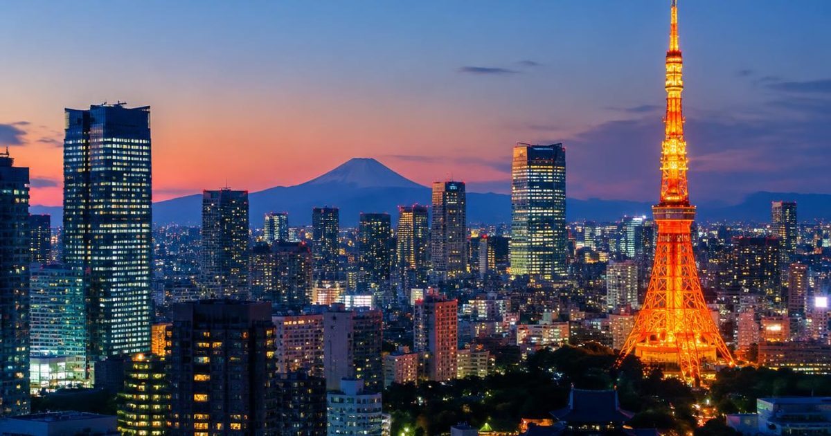 Tokyo Tower illuminated above a dense skyline at dusk, with a distant mountain silhouette