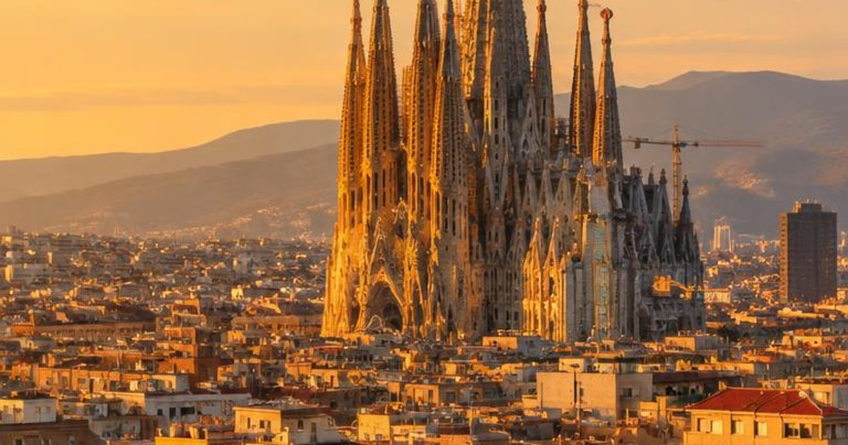 Sagrada Família rising above dense city buildings in warm evening light